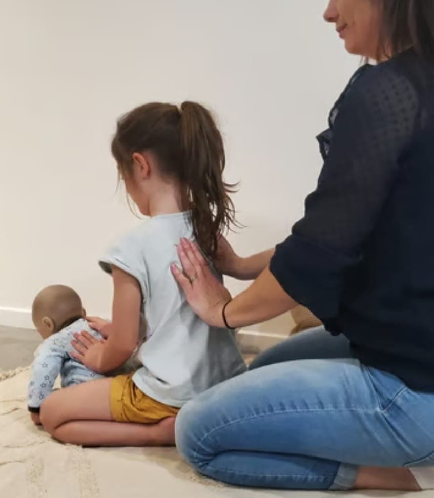 Un parent masse le dos de son enfant, qui masse à son tour son poupon